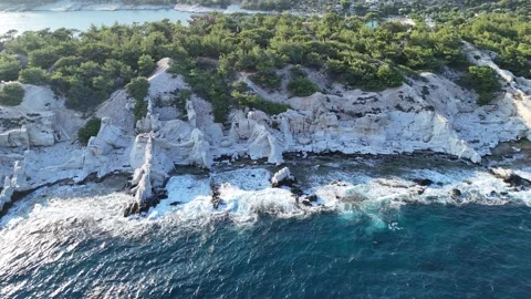 Vertical aerial view of waves hitting white marble coastal rocks. Video stock 327677620