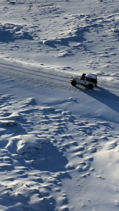 Vertical aerial view of a white off road vehicle driving along a snow covered Vídeos de archivo 334133749