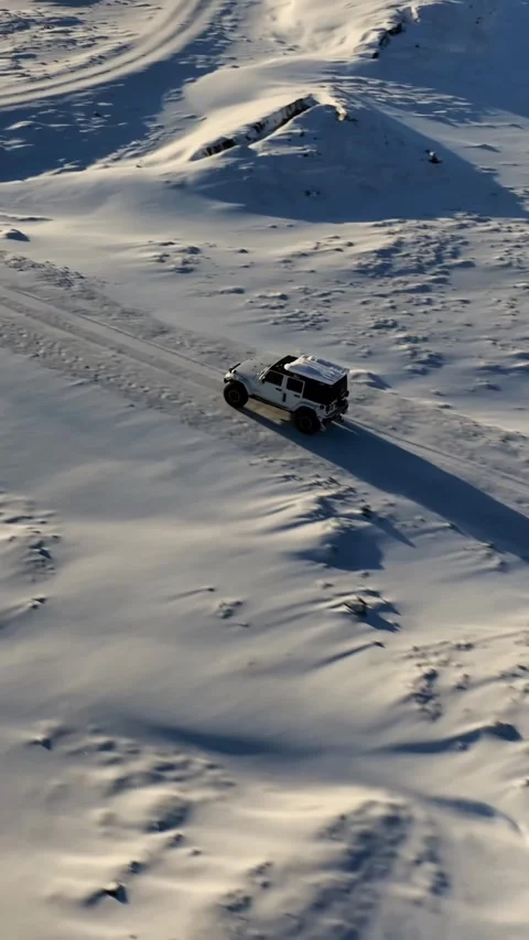 Vertical aerial view of a white off road vehicle driving across snowy volcanic Vídeo Stock 334133780