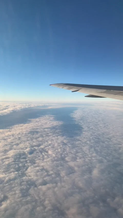 Vertical airplane window view above clouds in blue sky during flight Stock Footage 345213244