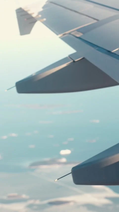 Vertical airplane window view of an aircraft wing above blue sea and small Video stock 334021414