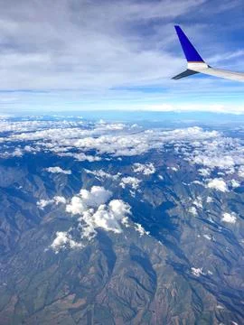 Vertical airplane window view flying over high mountain range under clear b.. Stock Photos