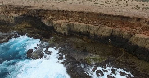 Vertical ascent fron low level of Waves Breaking on a rugged cliff shoreline Video stock 92843607