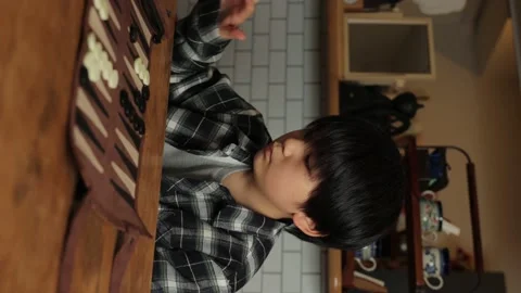 Vertical : Asian boy playing Backgammon at home. Playing black piece. Stock Footage 221360273