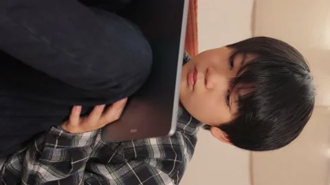 Vertical : Asian boy watching online video with his tablet computer on the sofa. Stock Footage 221356331