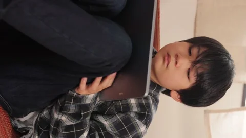Vertical : Asian boy watching online video with his tablet computer on the sofa. Stock Footage 221379656
