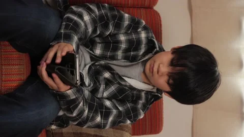 Vertical : Asian young boy playing online game with his smartphone on the sofa. Stock Footage 221355436