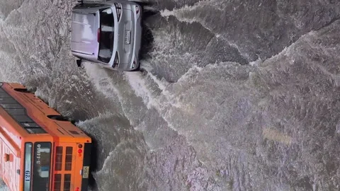 Vertical: Autos drive through flood water on inundated city street Stock Footage 346926860