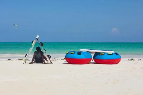 Vertical back view of a man in shade of boards sitting down facing the ocean. 写真素材
