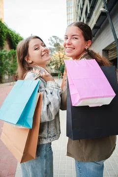 Vertical. Back view of two cheerful girls holding shopping bags while looking at Foto stock