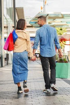 Vertical back view of young couple shopping on a mall, carrying paper bags in Stock Photos