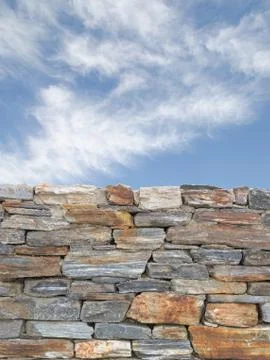 Vertical background with rough stone wall and blue cloudy sky Stock Photos
