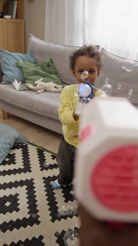 Vertical of Black Boy Playing with Soap Bubble Gun at Home with Father Stock Footage 345493093