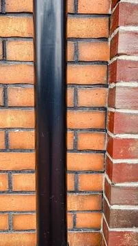 Vertical black downspout pipe installed on a textured red brick wall of a m.. Stock Photos