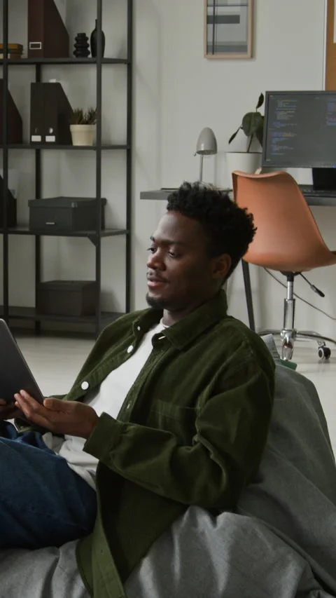 Vertical of Black Male Programmer with Laptop Sitting Down in Bean Bag Chair Video stock 335937644