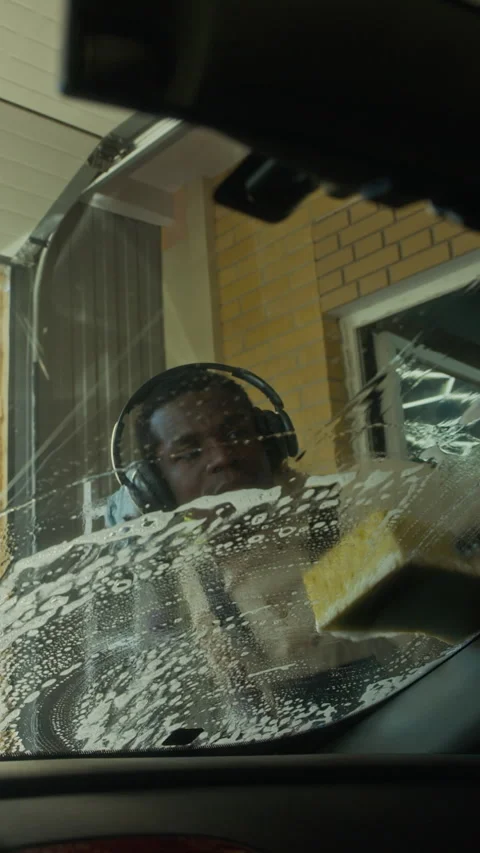 Vertical of Black Man Cleaning Car Windshield with Soapy Sponge Stock Footage 317307217