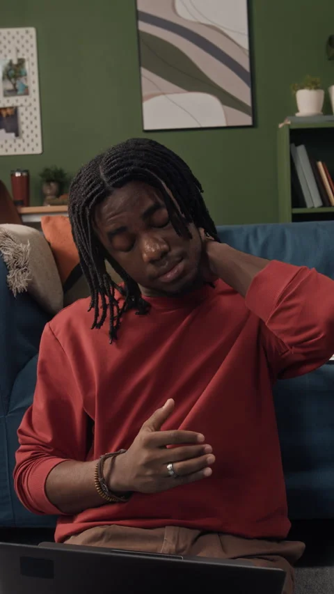 Vertical of Black Man Stretching Neck while Working Remotely on Laptop at Home Stock Footage 328249490