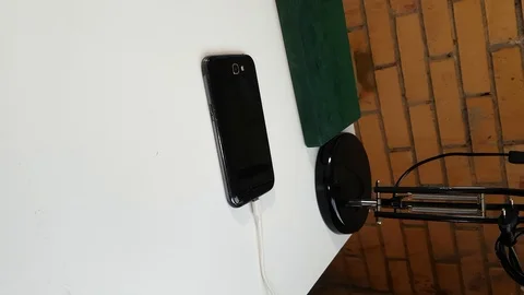 Vertical black smartphone explodes while charging on white table. Stock Footage 125432591
