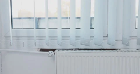 Vertical blinds gently wave when exposed to heated air from the radiator. Video stock 228423720