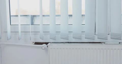 Vertical blinds gently wave when exposed to heated air from the radiator. Video stock 229288618