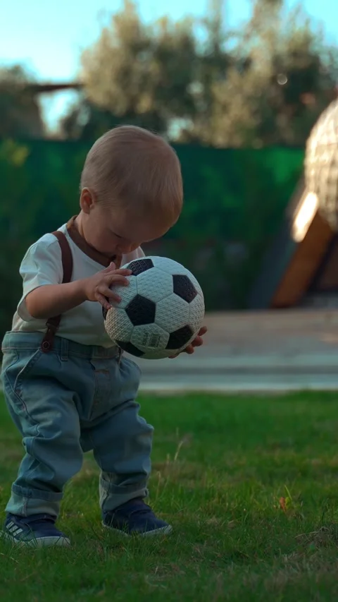 Vertical of Blond boy picks up soccer ball walking on green grass Stock Footage 275671677