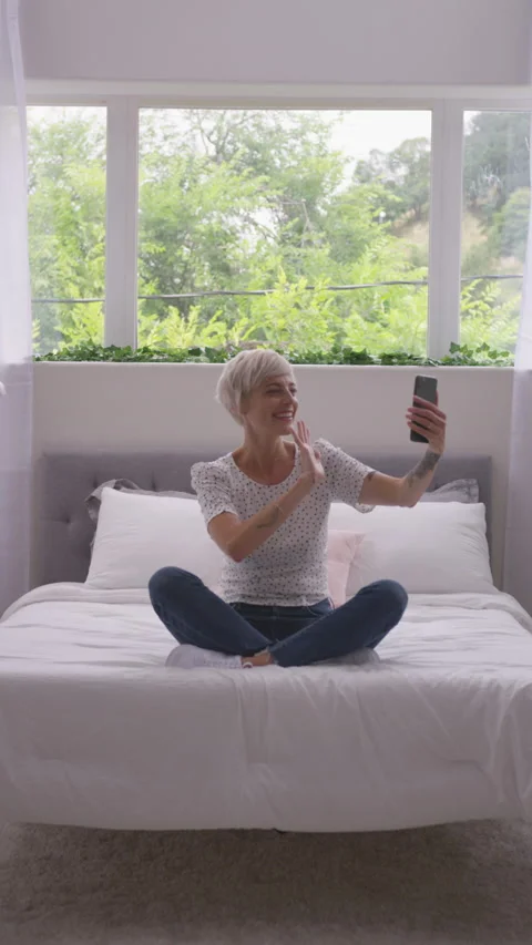 Vertical of Blonde with Pixie Haircut Smiling and Waving as She Skypes From Bed Stock Footage 208778254