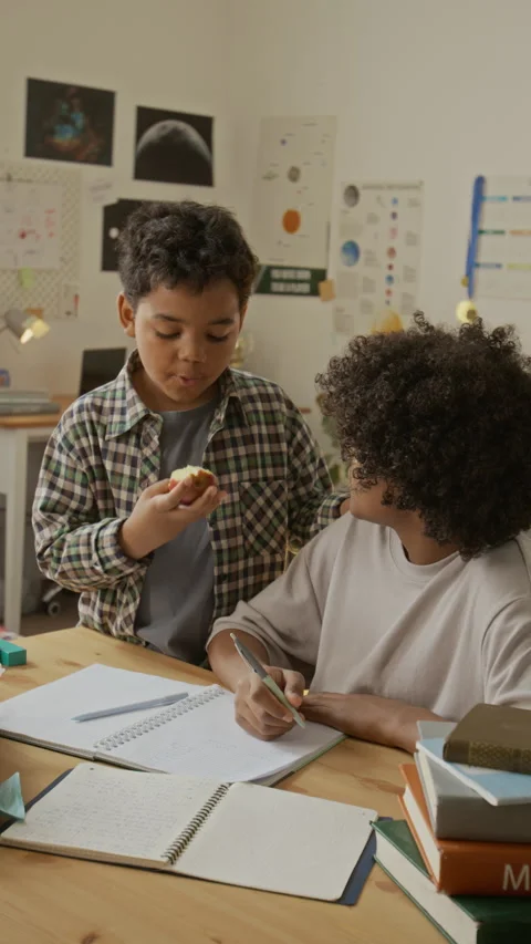 Vertical of Boy Eating Apple and Talking to Teenage Brother Doing Homework Stock Footage 342511227