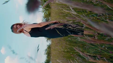 Vertical camera chasing a romantic girl in a dress walking across a field Stock Footage 246957915