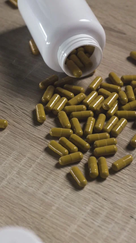 Vertical camera panning shot of yellow pills spilled from white bottle on table Stock Footage 342239933