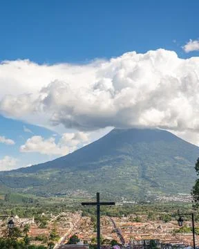 Vertical capture of volcano covered by clouds and cross towering over the c.. Photos