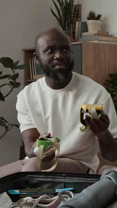 Vertical of Cheerful Black Man Trying on Dive Masks while Packing for Vacation Stock Footage 333293023