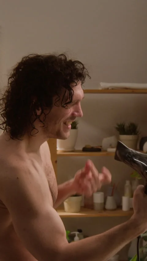 Vertical of Cheerful Man Having Fun Singing with Hair Dryer in Bathroom Stock-Footage 342728080