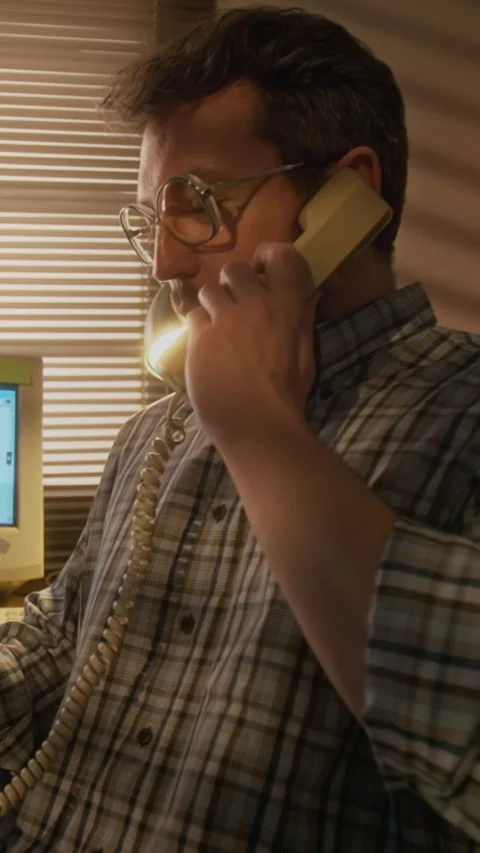 Vertical of Cheerful Man Talking on Corded Telephone by Retro Computer in Office Stock Footage 327239523