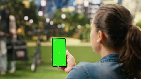 Vertical chroma key mockup on smartphone held by casual woman in city park Stock Footage 343500677