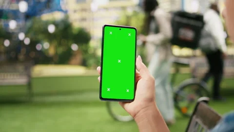 Vertical chroma key screen on mobile phone held against blurred urban park Vídeo Stock 343506884