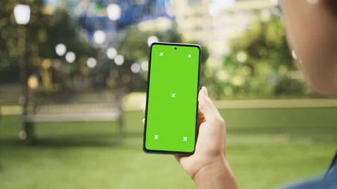 Vertical chroma key screen on mobile phone held against blurred urban park Stock Photos