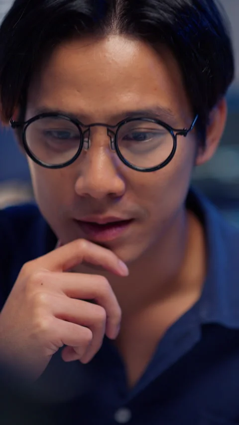 Vertical Close-up of Asian Man in Glasses Deeply Concentrating at Night. Stock Footage 322779054