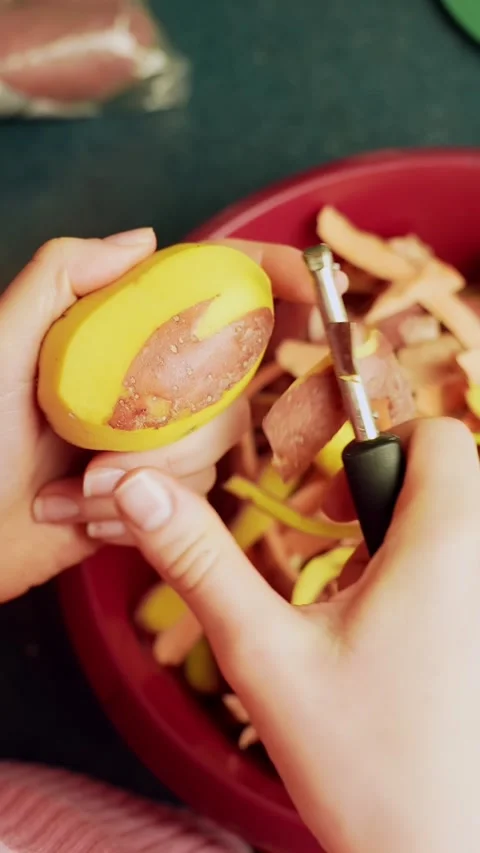 Vertical close-up of beginner hands peeling a potato with a swivel peeler over Video stock 331108208
