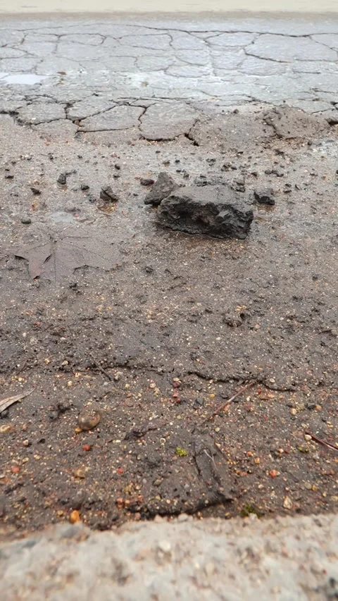 Vertical close-up of broken asphalt after winter with loose chunks and a Видео 333654071