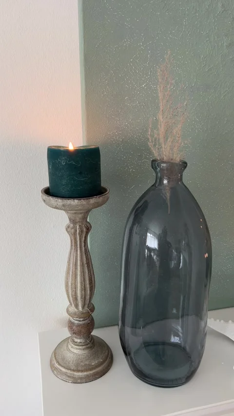 Vertical close up of burning green candle on wooden stand and glass vase decor Video stock 346486209
