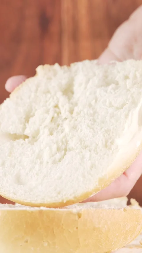 Vertical Close-Up of Butter Being Spread on Soft Bun Half on Wooden Blurred.. Vídeo Stock 312169077