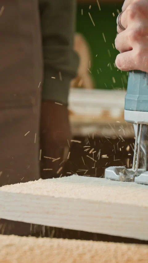 Vertical Close-Up of Carpenter Shaking Sawdust off Plank, Making Cut with Jigsaw Stock Footage 334416555