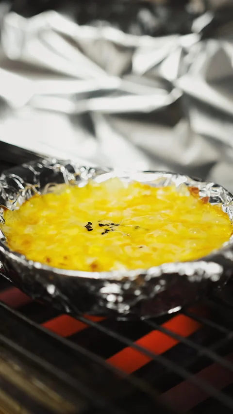Vertical close up of cheesy corn side dish bubbling on restaurant grill Video stock 333878903