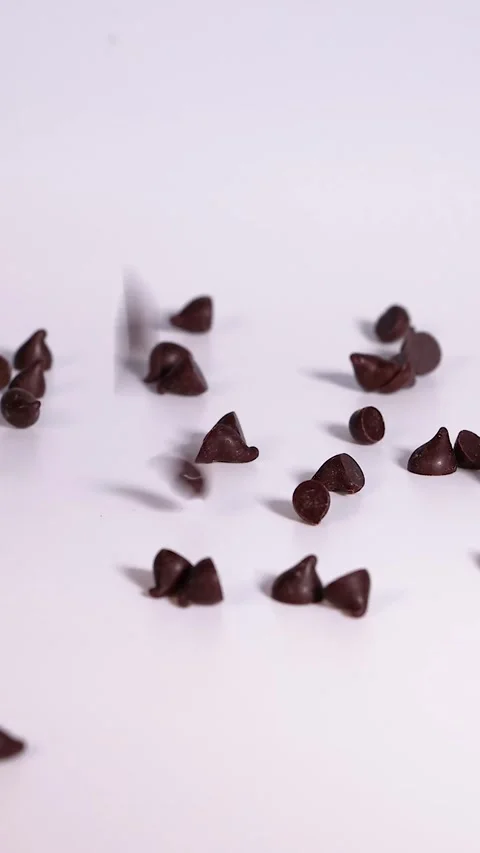 Vertical Close Up of Chocolate Chips Falling on White Surface Stock Footage 325760256