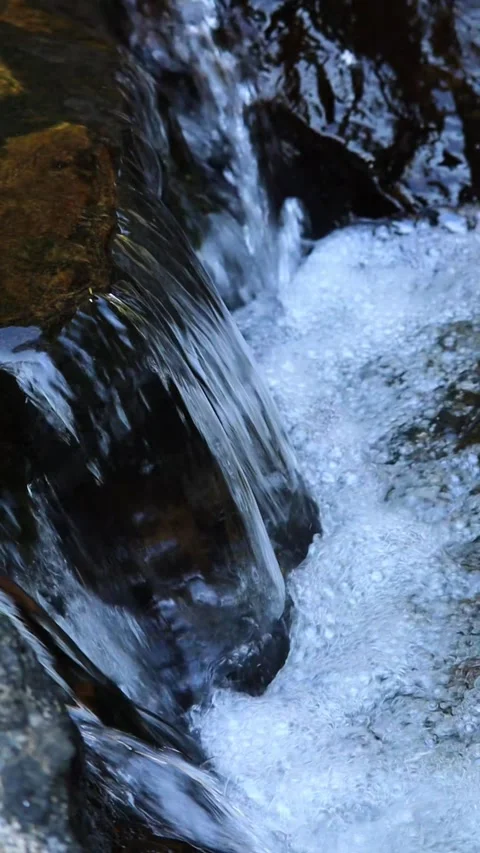 Vertical close-up of clear water cascading over rocks in a natural forest stream Stockbeeldmateriaal 346868829