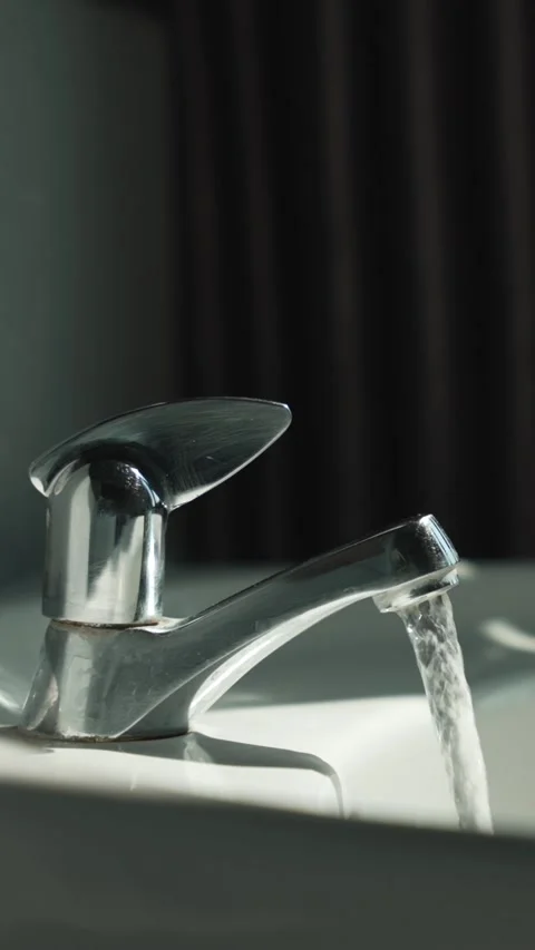 Vertical close up of clear water stream pours into the sink from a chrome mixer Video stock 316587844