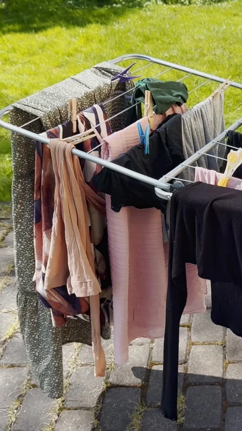 Vertical close-up of clothes drying on a metal rack outdoors, with clothespins Stock Footage 338004232