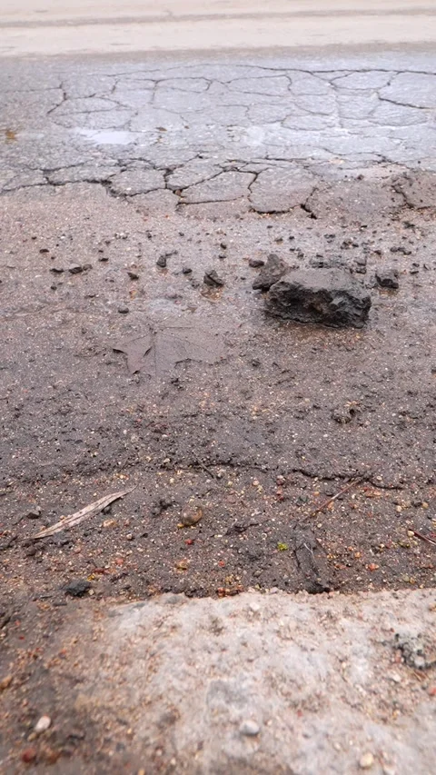 Vertical close-up of crumbling asphalt with loose road pieces and a passing car Stock Footage 333655834