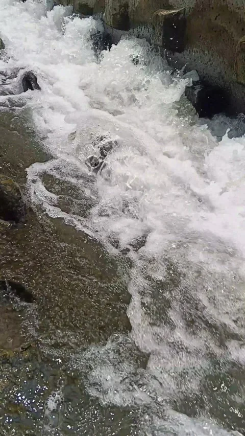 Vertical close-up of fast-flowing water splashing with white foam over stone Video stock 346766699