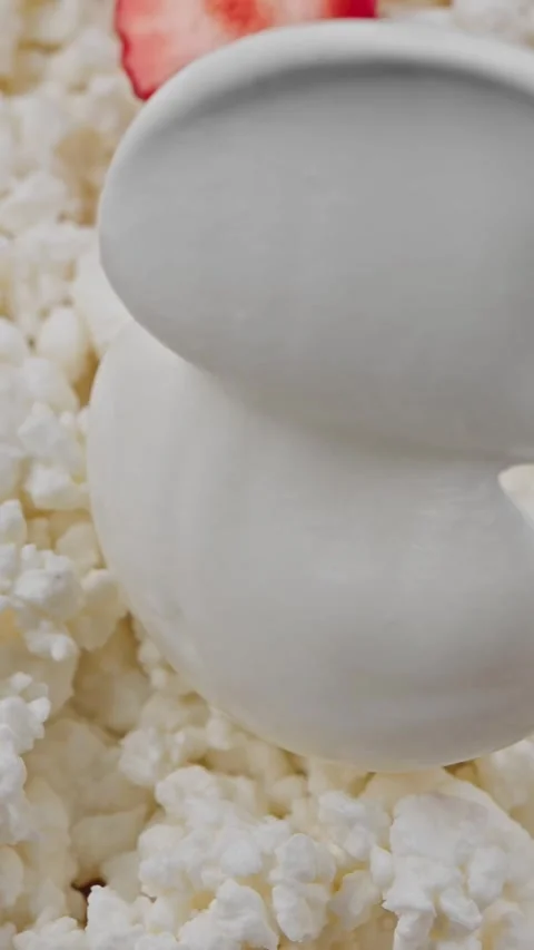 Vertical close-up of fresh cottage cheese topped with a spoonful of sour cream Stock Footage 318474931